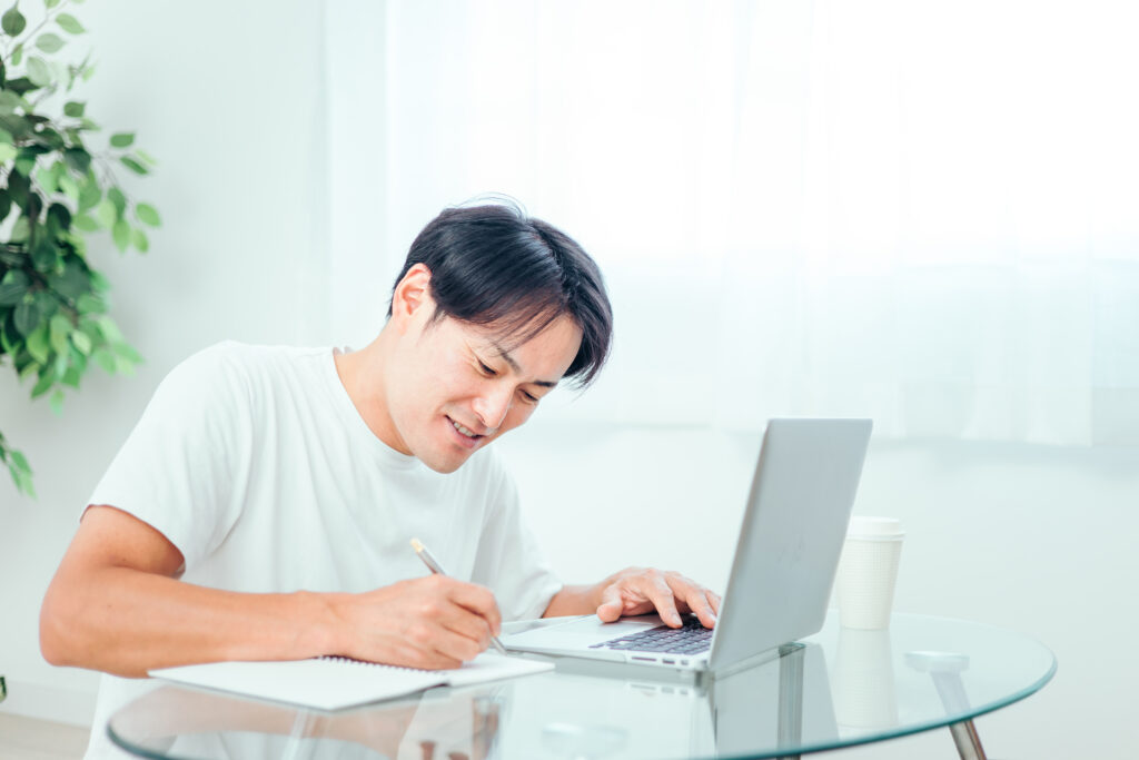 家でパソコンを使って勉強する男性(笑顔)