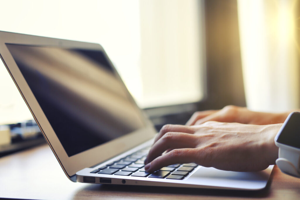 窓際でラップトップを使用する人物の手元クローズアップ 背景ぼかし