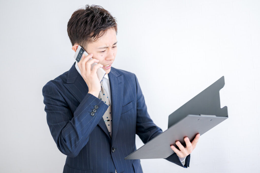 書類を見て電話するスーツ男性