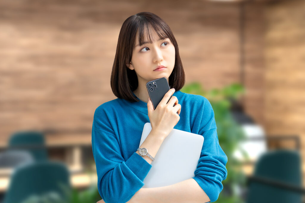 スマホとパソコンを持って考える女性