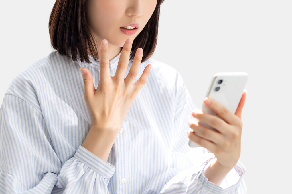 スマホの画面を見て驚く女性