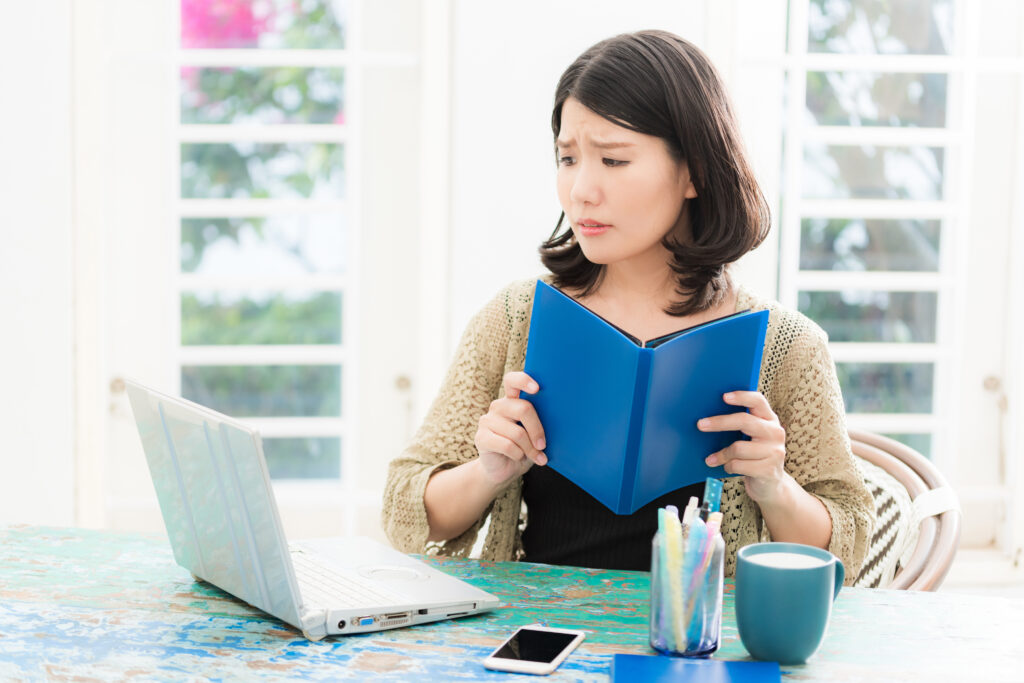 パソコンの前に座り本を持っている女性