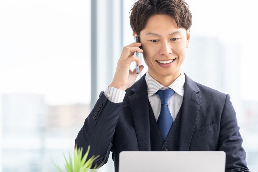 パソコンを見ながら電話をする男性
