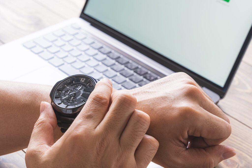 パソコンの前で時計を見る男性の手