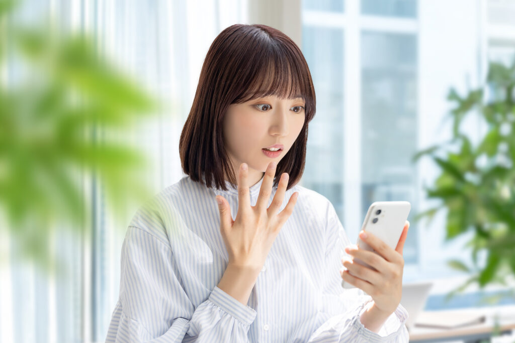 スマホの画面を見て驚く女性