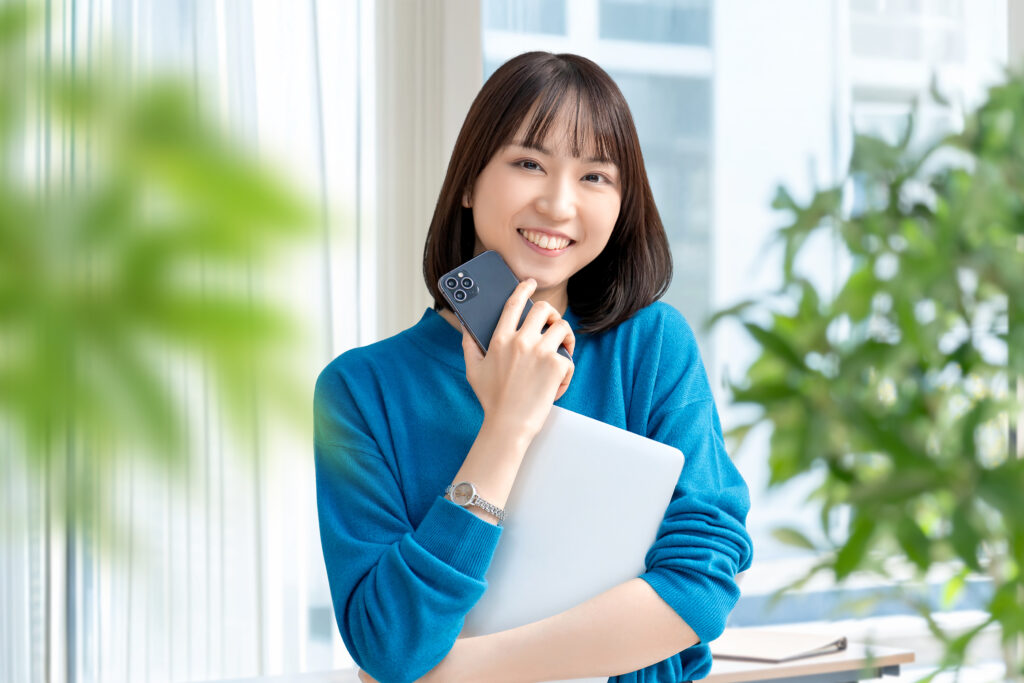ノートパソコンとスマホを持つ笑顔の女性