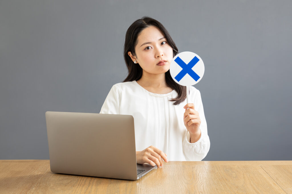 バツ印を出すPC前のアジア人女性