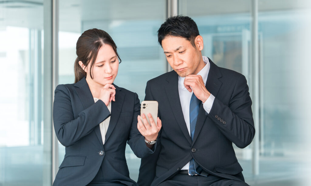 スマホを見て悩むスーツ姿の男女