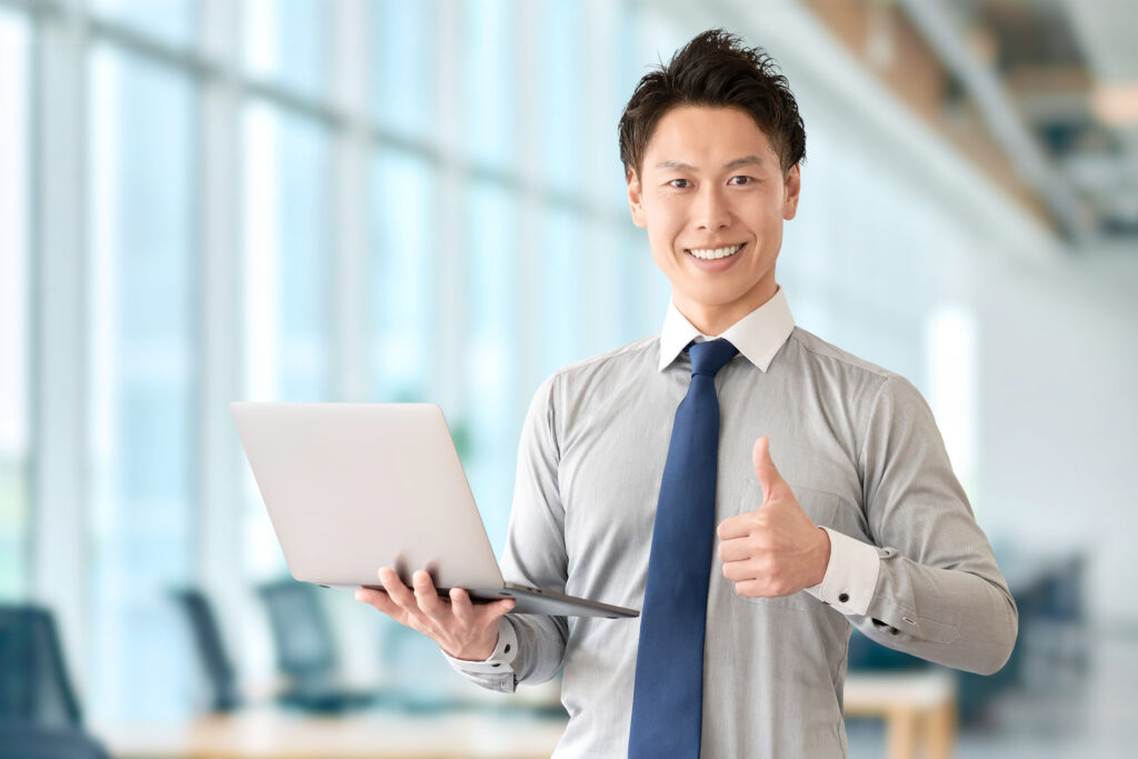 パソコンを持っていいねのポーズをする男性