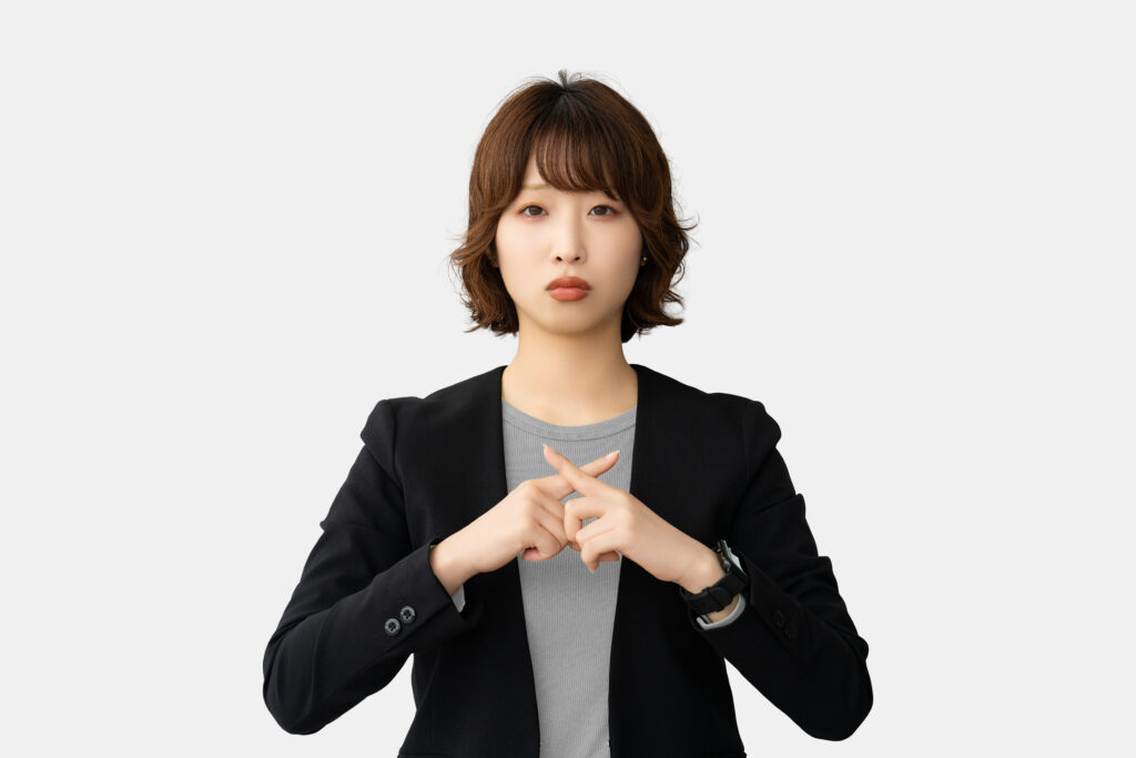 指でバツのポーズをする困った表情の女性