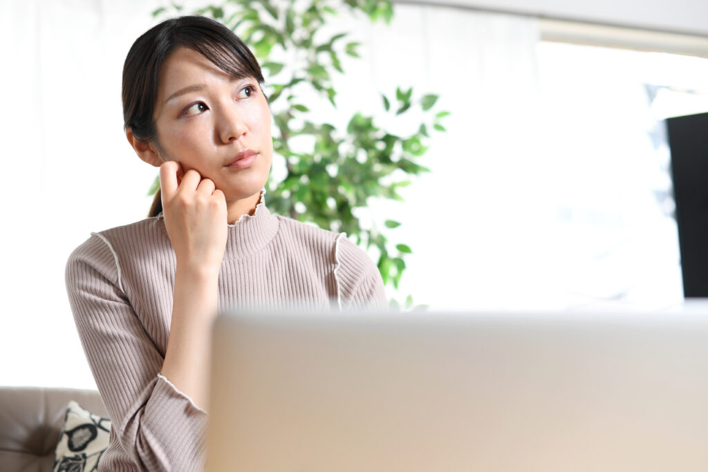 ノートパソコンの前で悩む若い女性