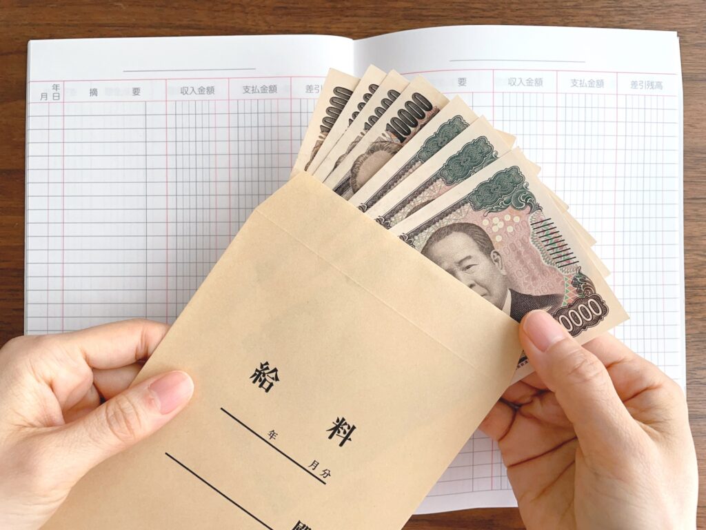 机上の家計簿と給料袋から紙幣を取り出す手