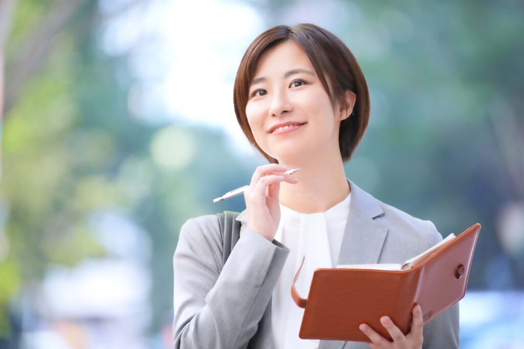 ペンと手帳を持ち遠くを見る女性