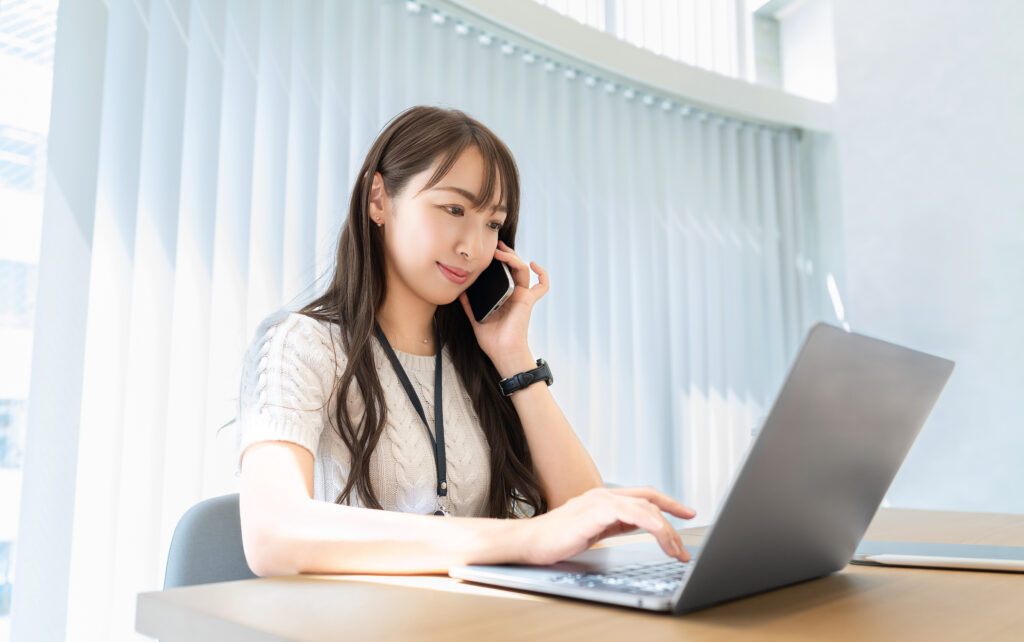 スマホで話しながらパソコンを使う女性