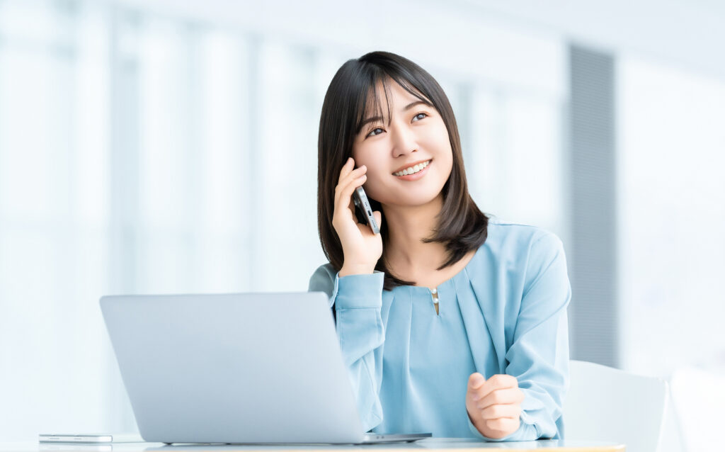 パソコンを使いながらスマホで話す女性