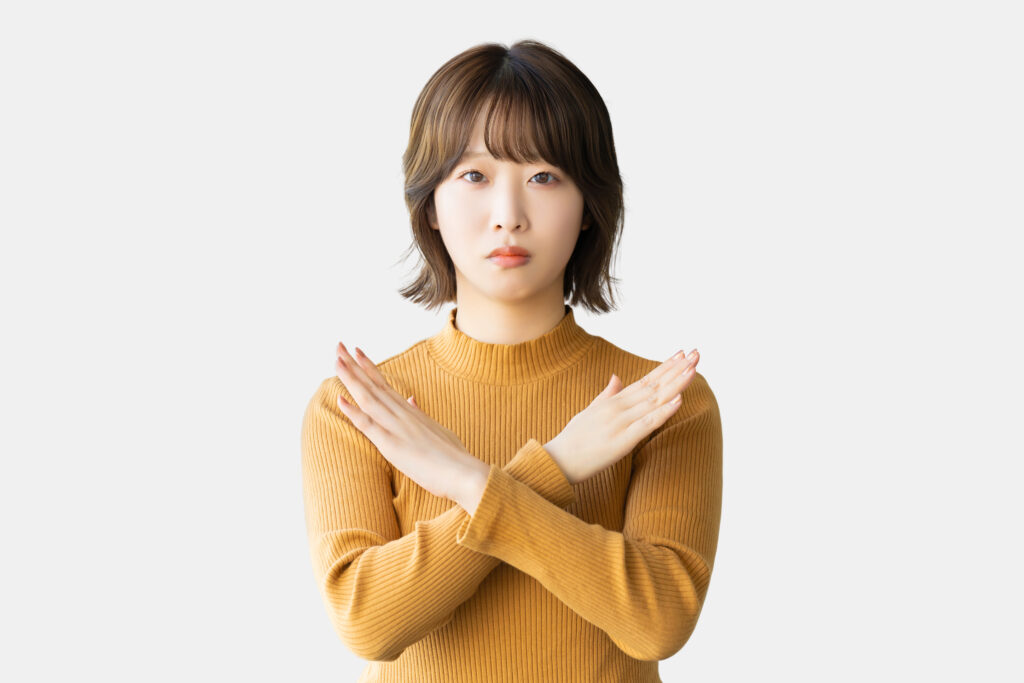 手でバツのポーズをする困った表情の女性