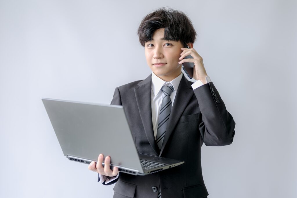 パソコンを持って電話する男性