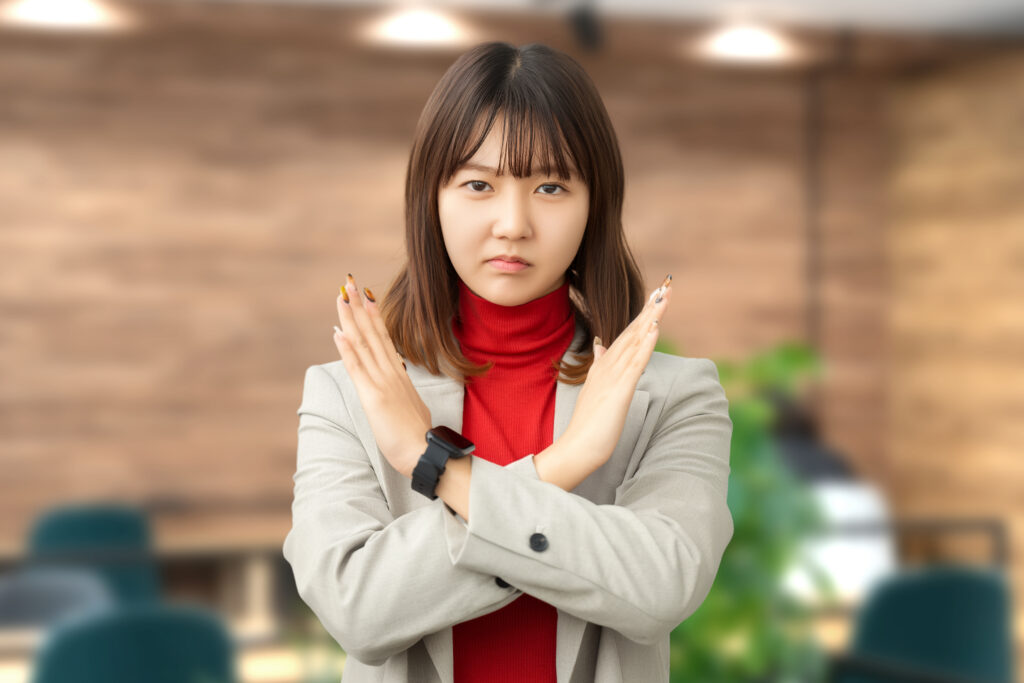 手でバツのポーズをする困った表情の女性