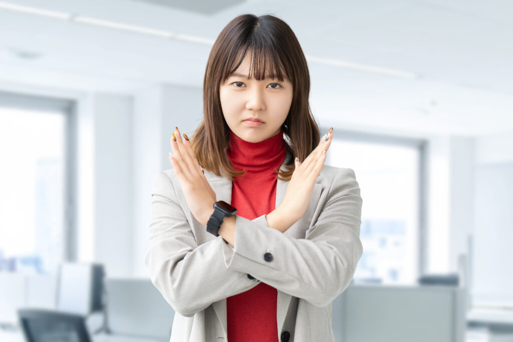 手でバツのポーズをする困った表情の女性