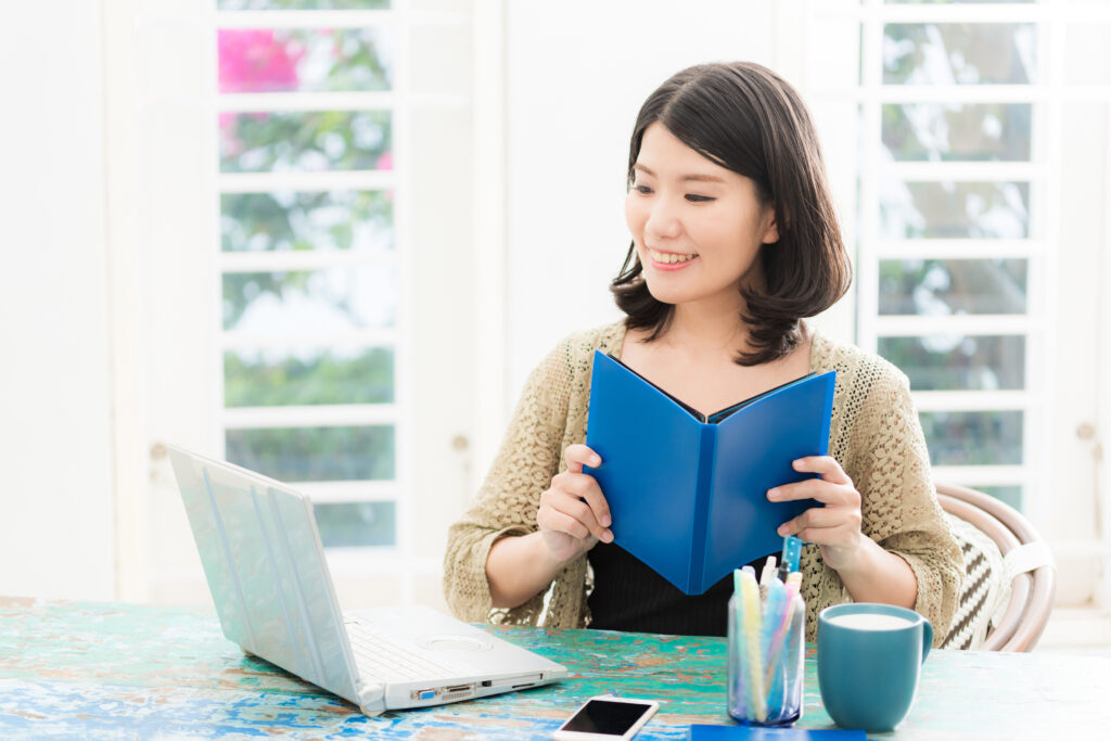 パソコンの前に座り本を持っている女性
